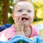 Portrait of Cute baby boy with Down syndrome lying on blanket in summer day on nature with toys